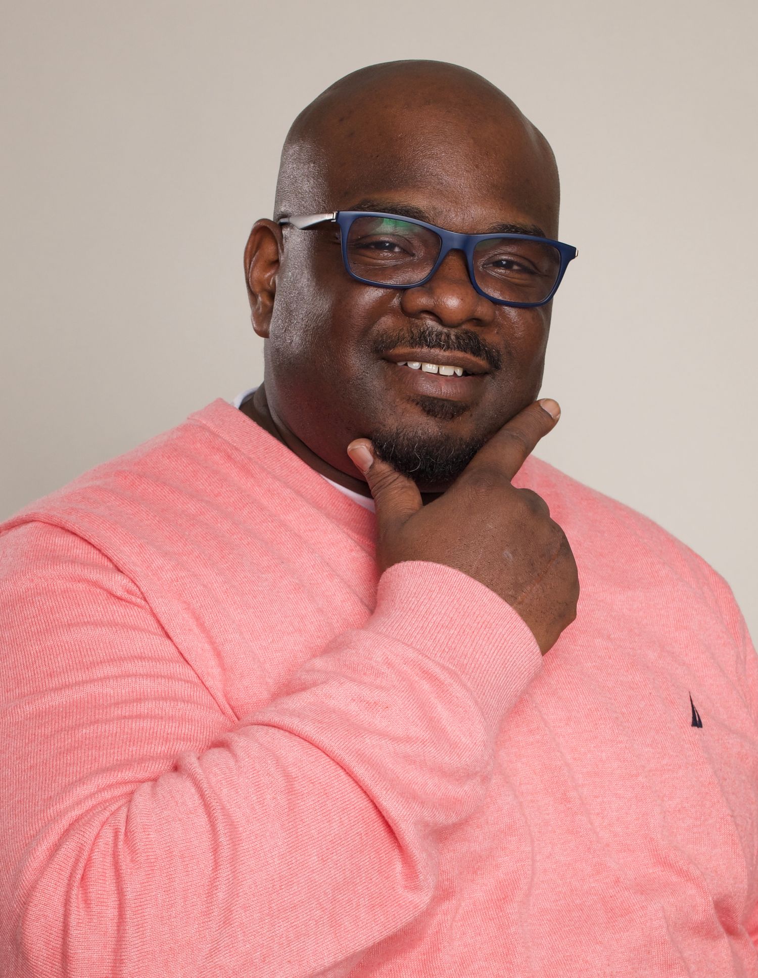 Professional portrait with person in pink sweater and blue glasses smiling.
