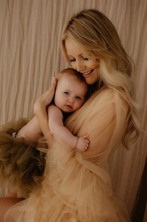 Intimate moment between parent and infant captured in soft beige tones with tulle dress details.