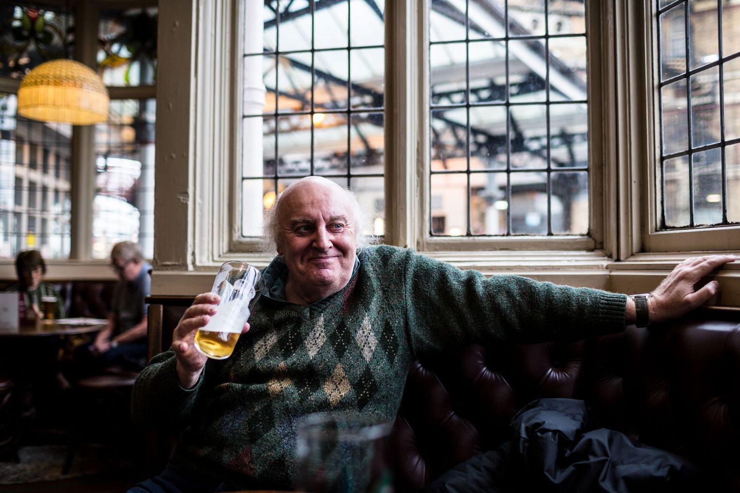 Cheerful patron enjoying a drink by window in traditional British pub setting.