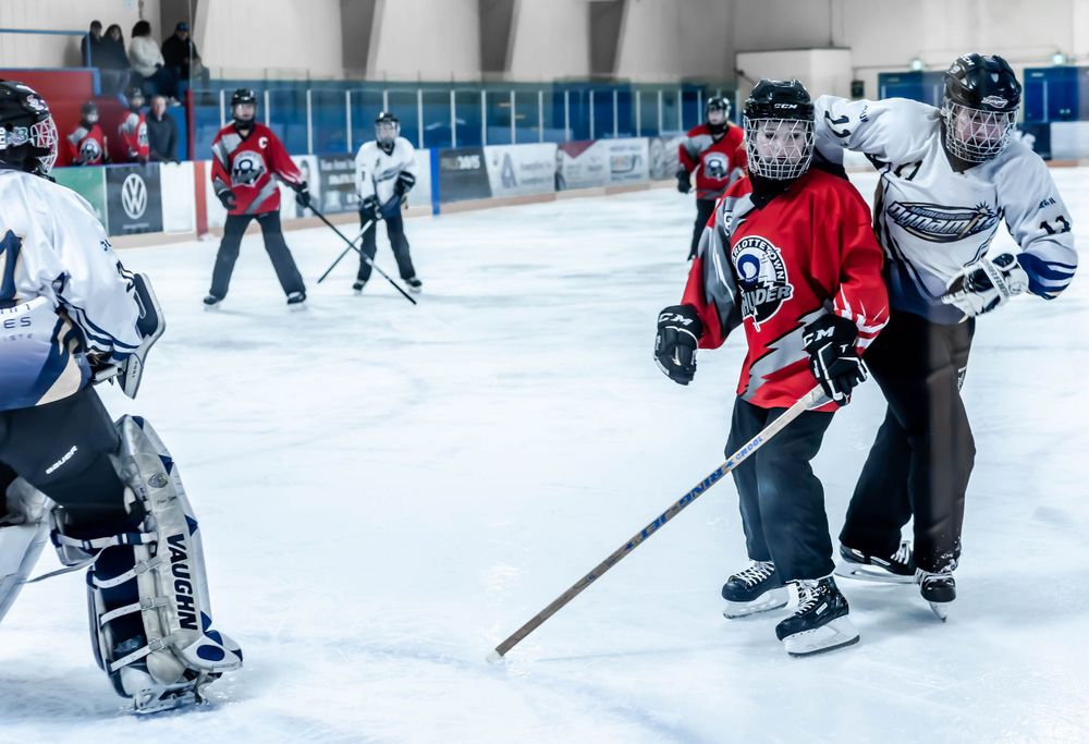 Hockey players in red and blue jerseys facing off on an ice rink during a match.