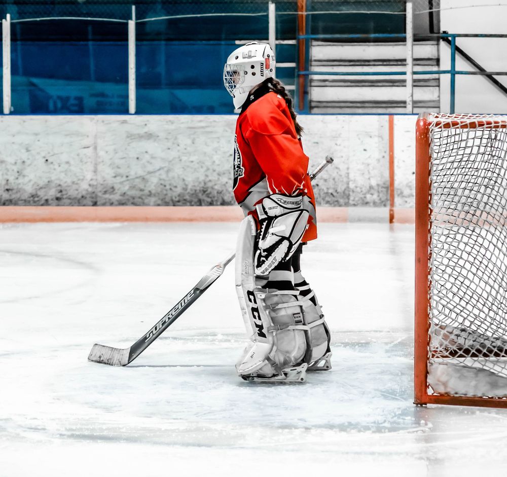 Hockey goalie in red jersey stands ready at the net during a game.