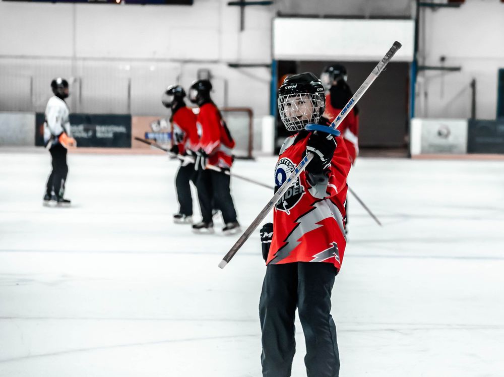 Hockey player in red jersey raises stick while practicing on indoor ice rink.
