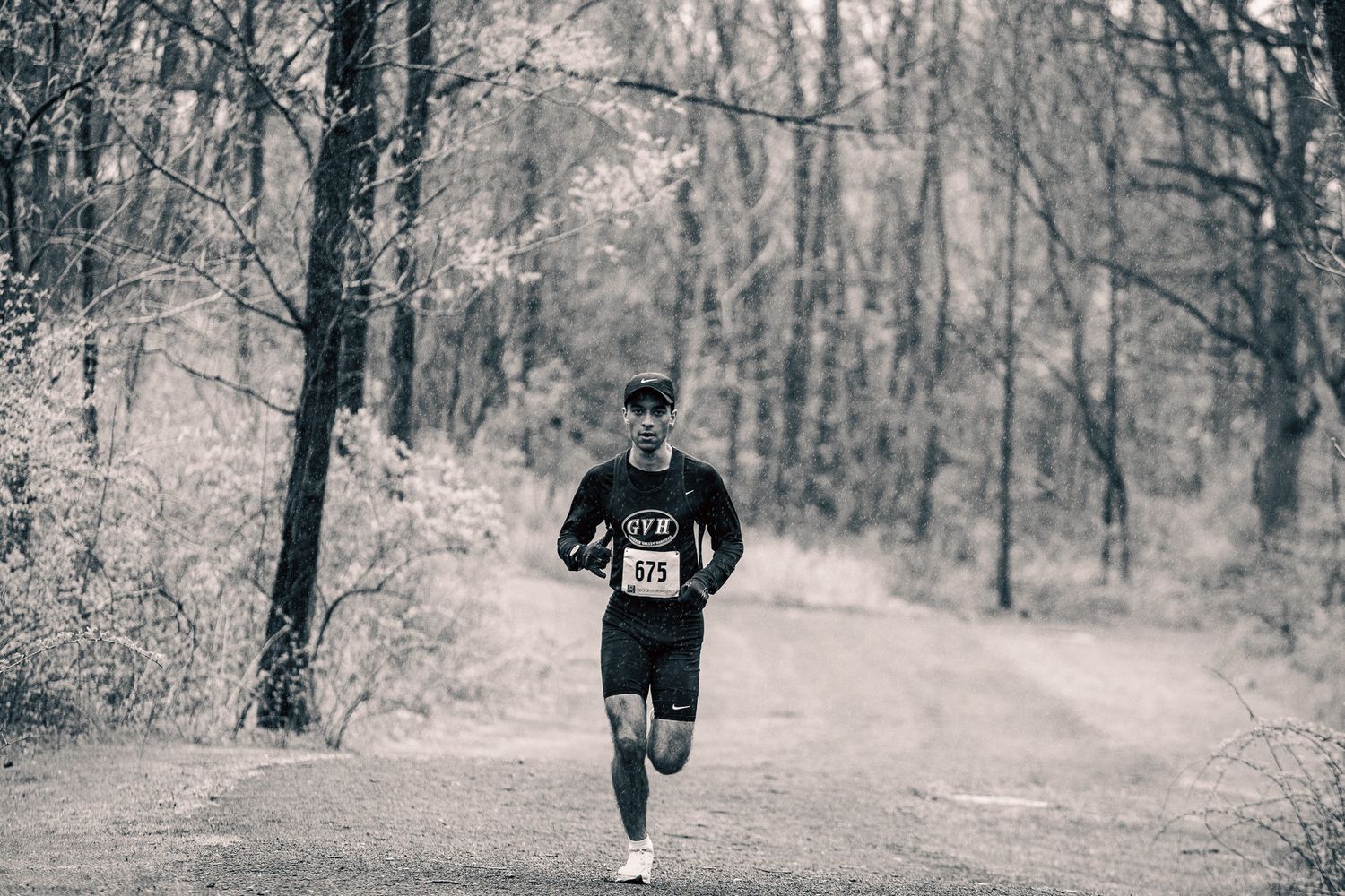 Black and white photo of runner on forest trail during winter season.
