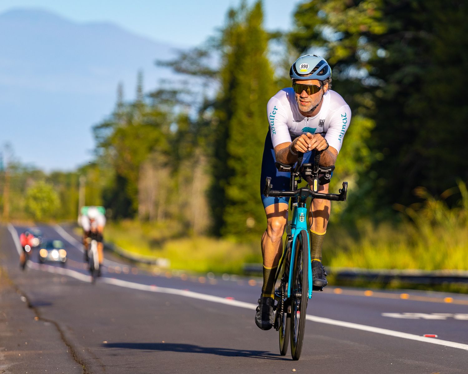 Cyclist in white jersey riding time trial bike on mountain road.