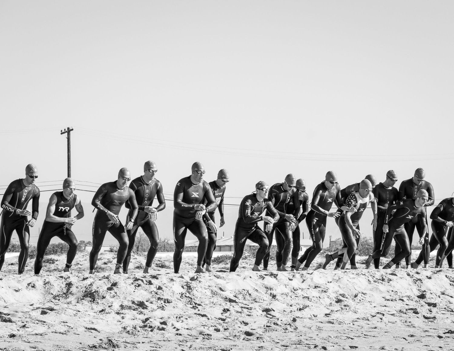 Group of wetsuit-clad swimmers lined up on beach preparing for ocean race start.