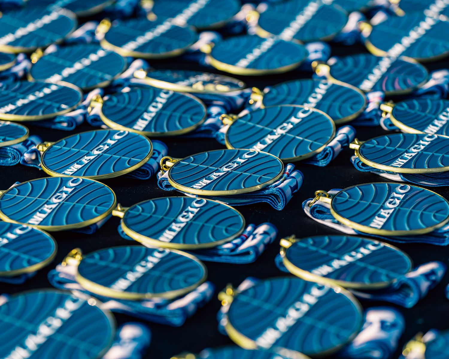 Rows of blue circular race medals with ribbons laid out in a repetitive pattern.