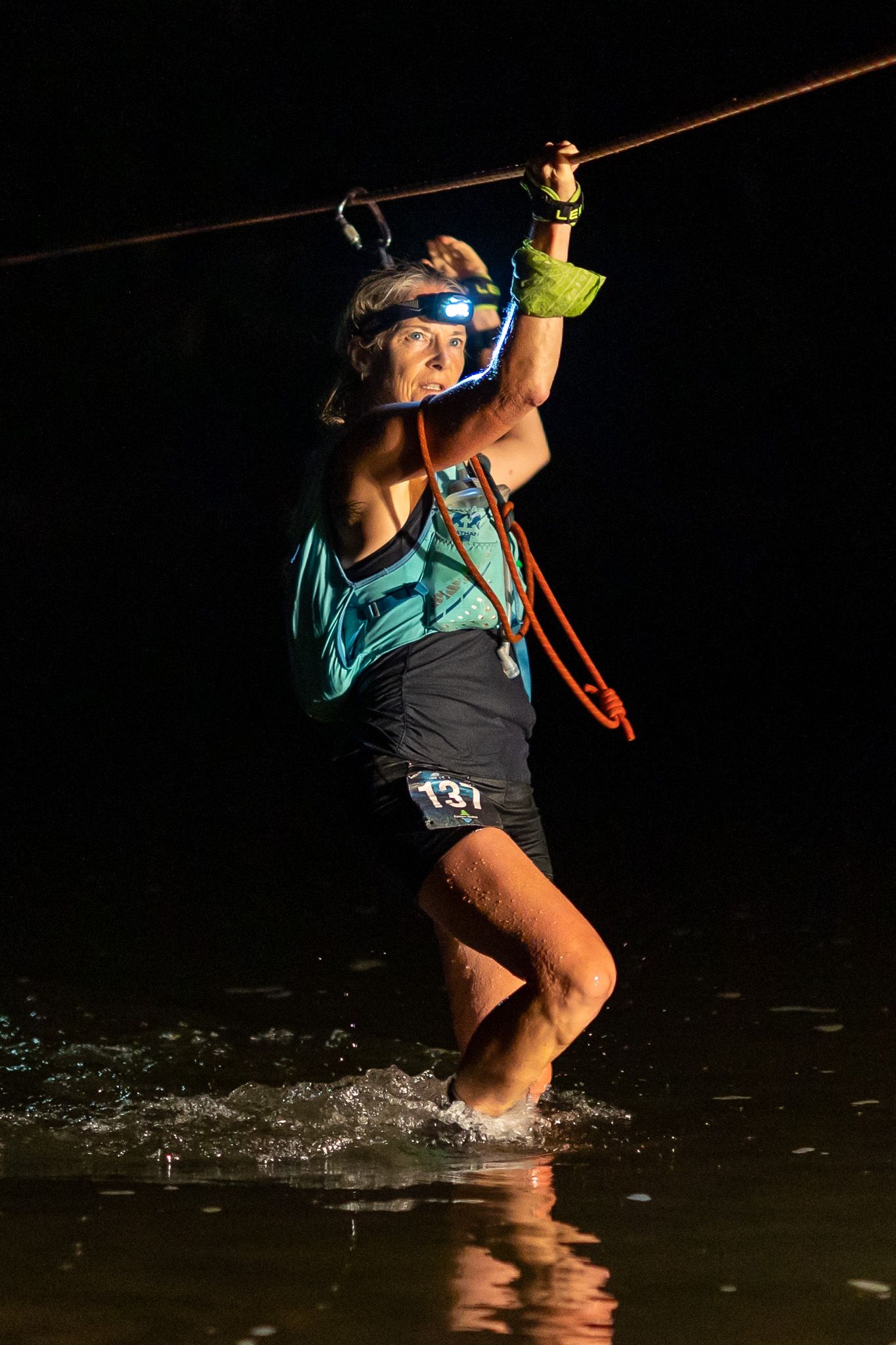 Adventure racer crossing a water obstacle at night using ropes and safety gear.