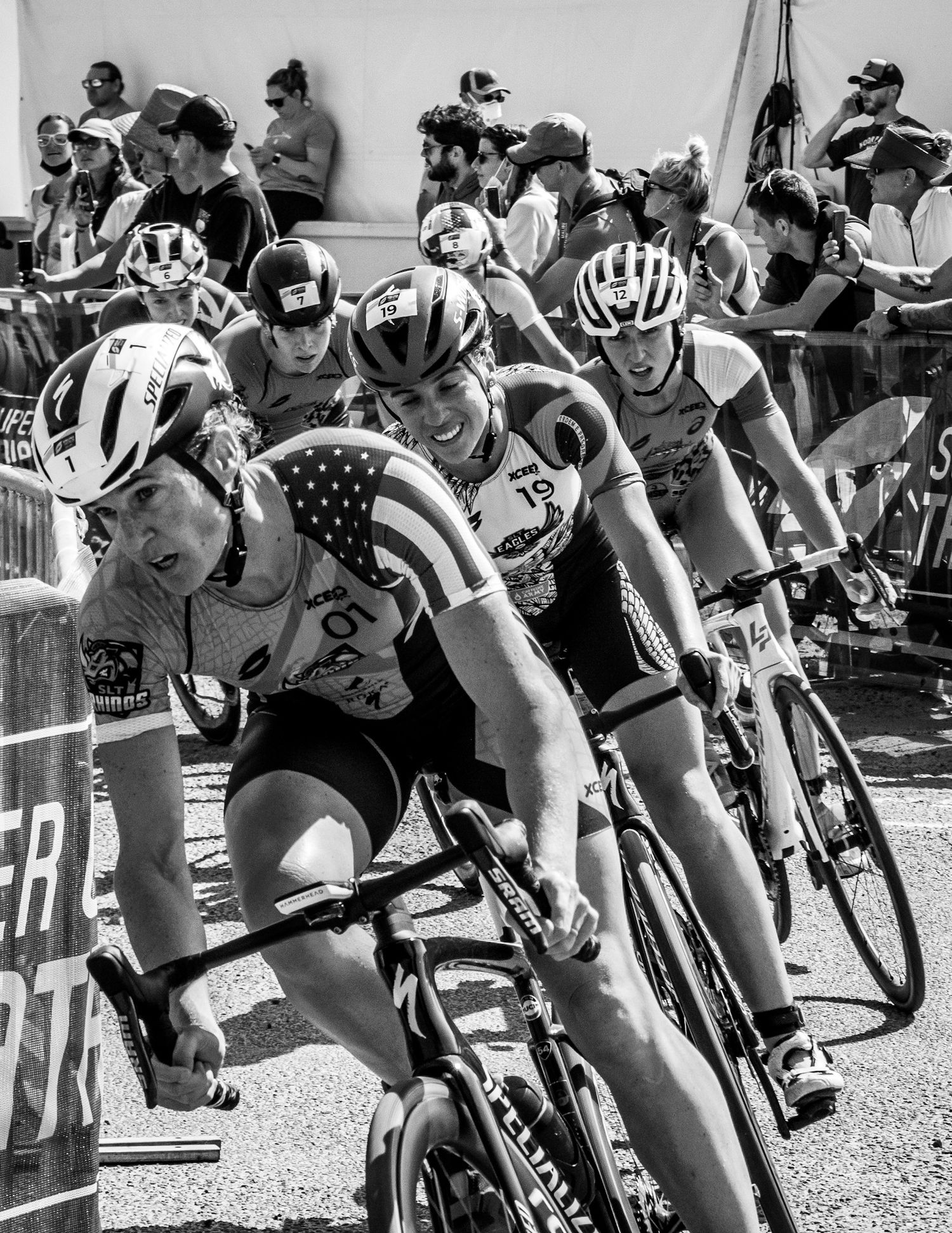 Cyclists racing in a competitive road cycling event wearing American flag jerseys and helmets.