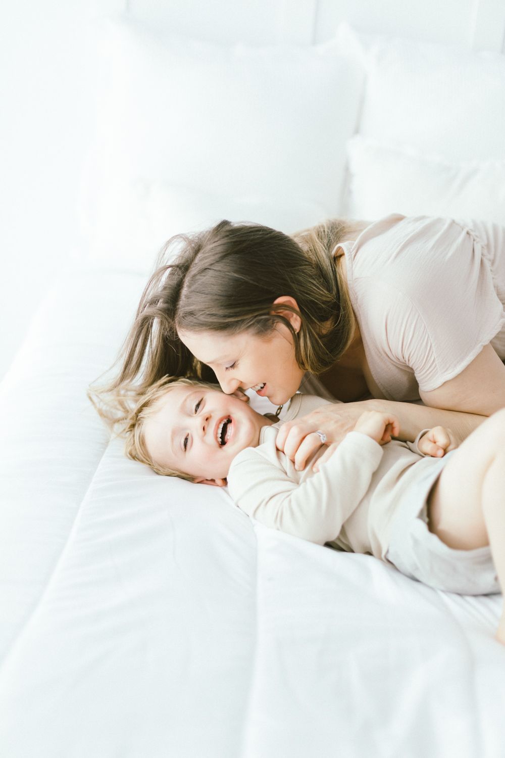 Tender embrace between parent and child on white bedding in soft lighting.