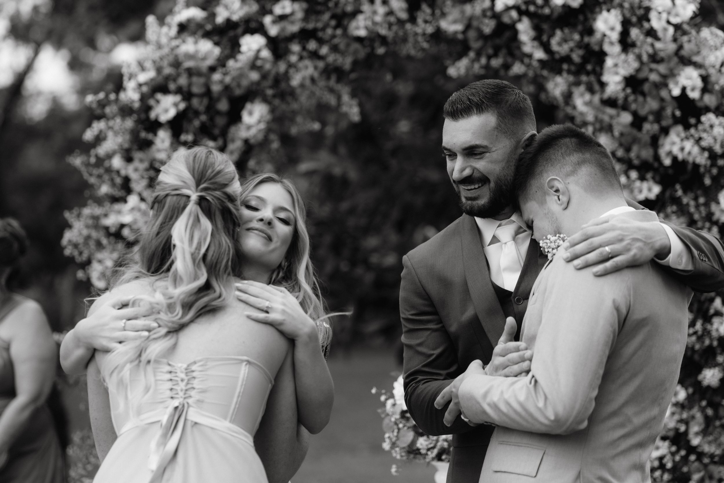 A joyful embrace during an outdoor wedding ceremony with white flowers in the background.
