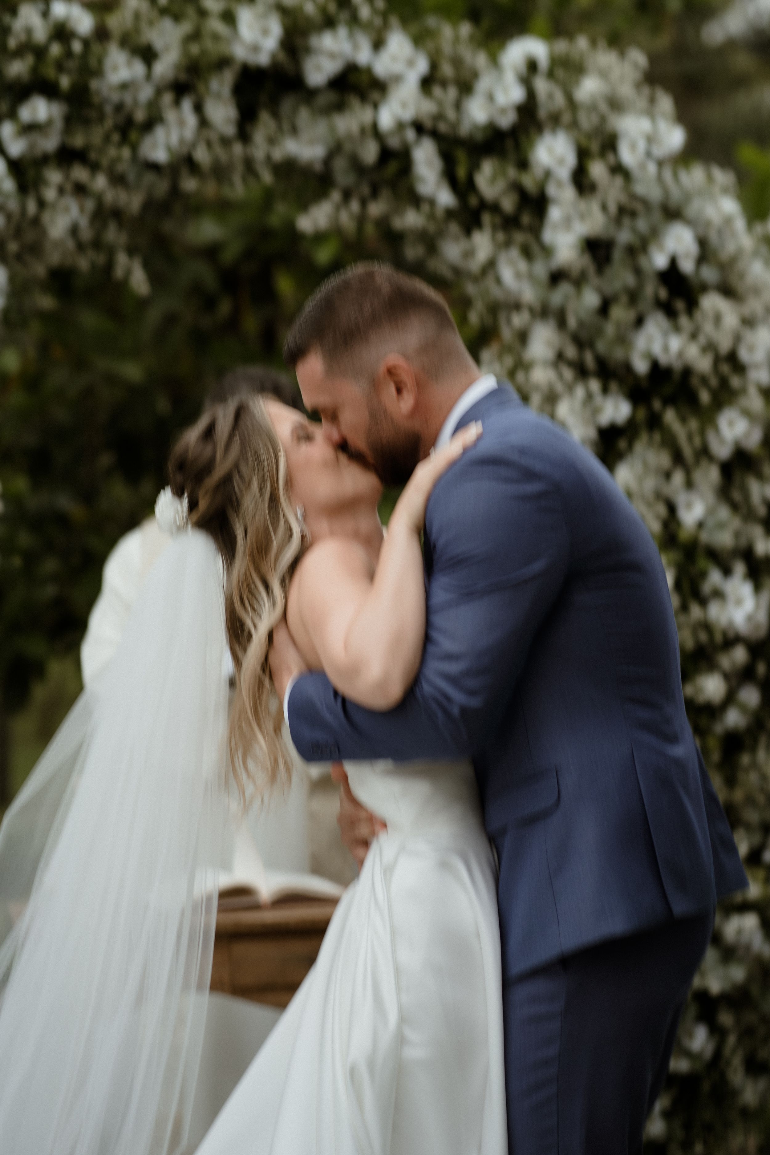 A romantic first kiss between newlyweds at an outdoor wedding ceremony.