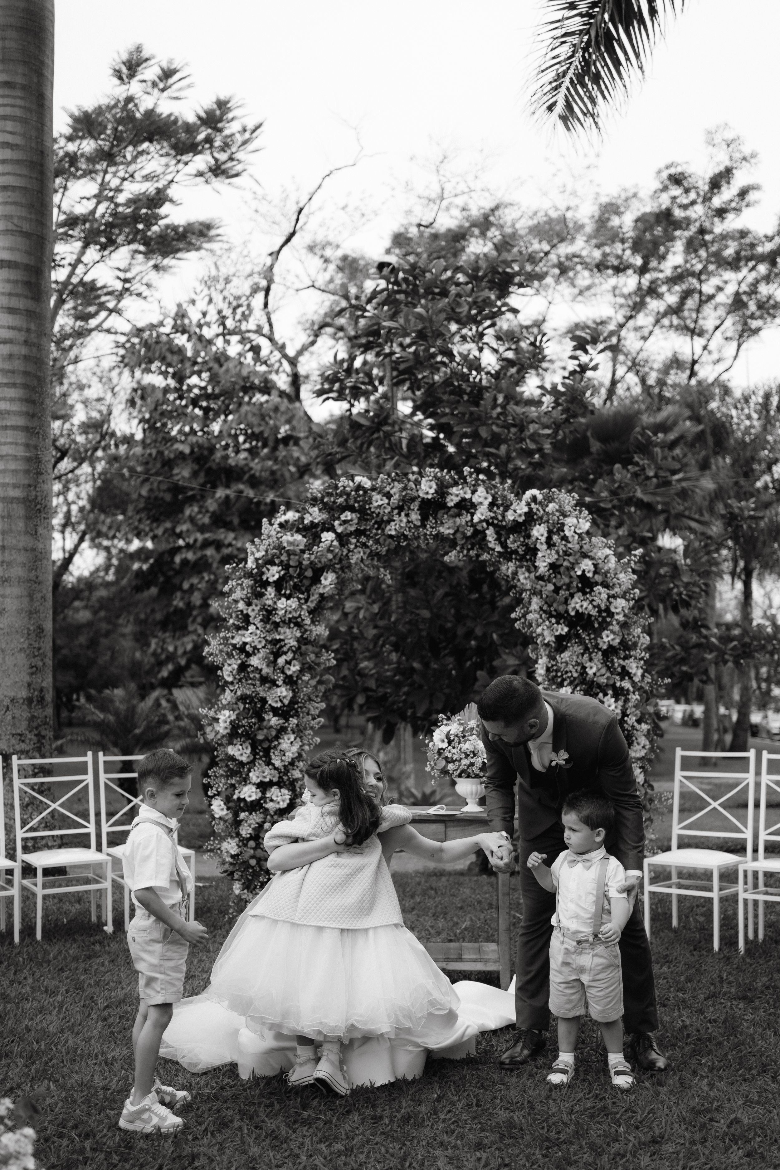 Children in white outfits playing on the grass during a wedding ceremony.