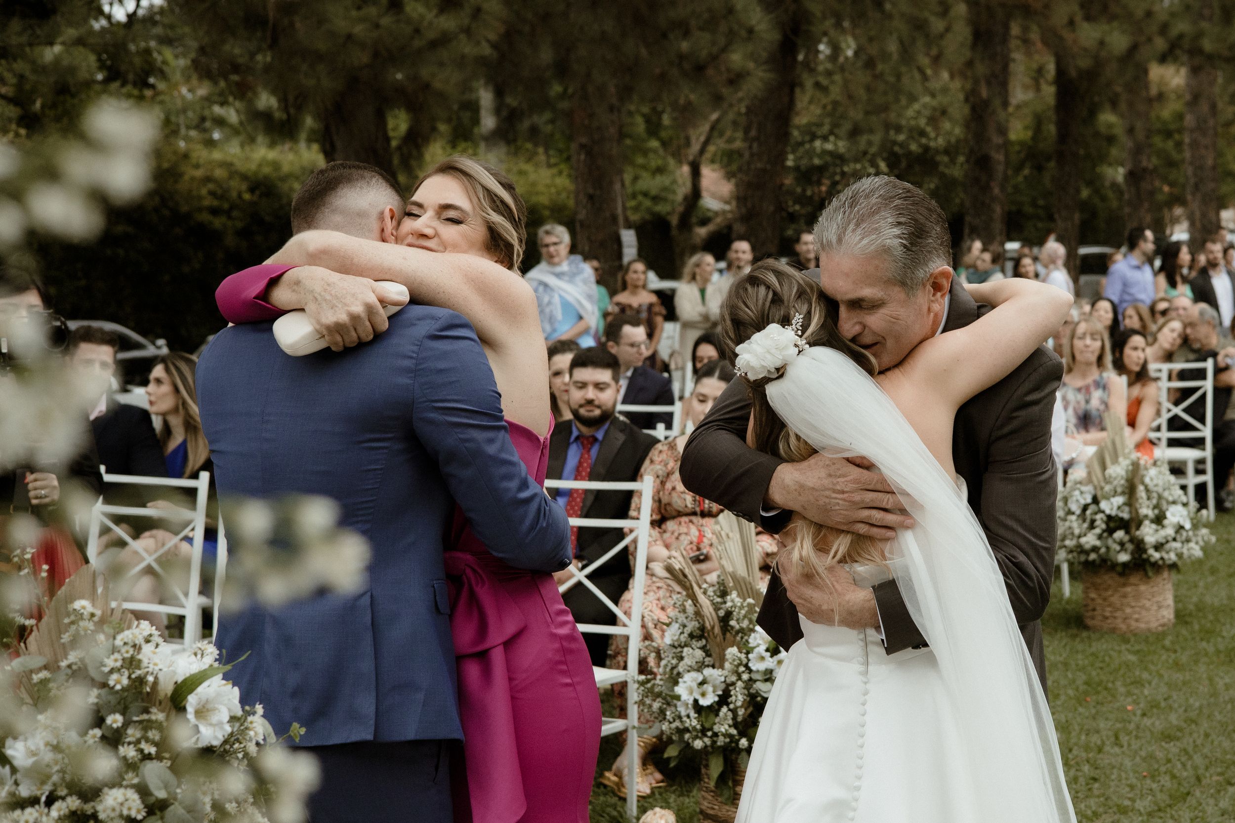 Emotional hugs shared between wedding couple and family members during outdoor garden ceremony.