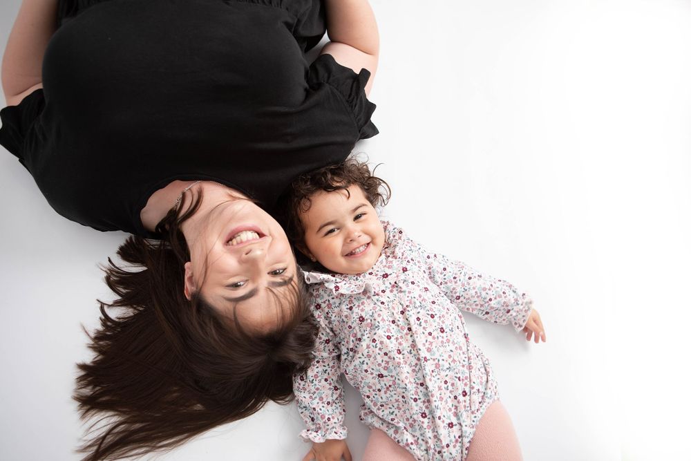 Overhead view of smiling mother and laughing baby lying together on a white background.