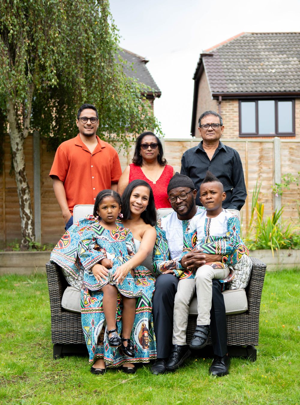Multi-generational family in colorful African print outfits posing together in a sunny garden.