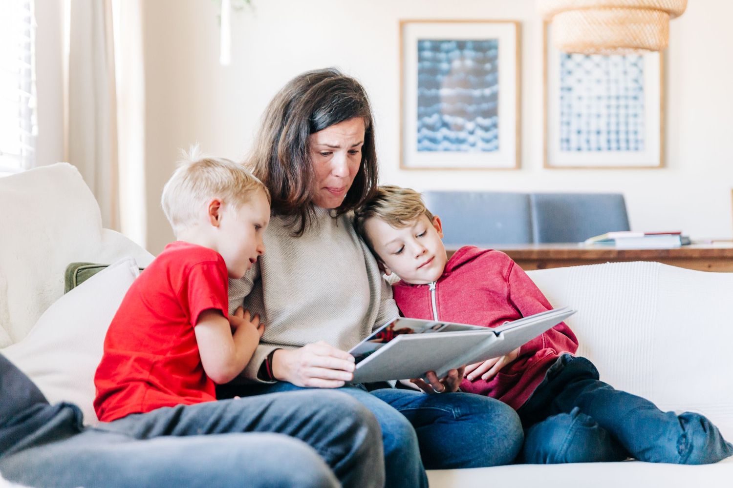 Mother sitting with her sons on the couch, crying happy tears at a photo album
