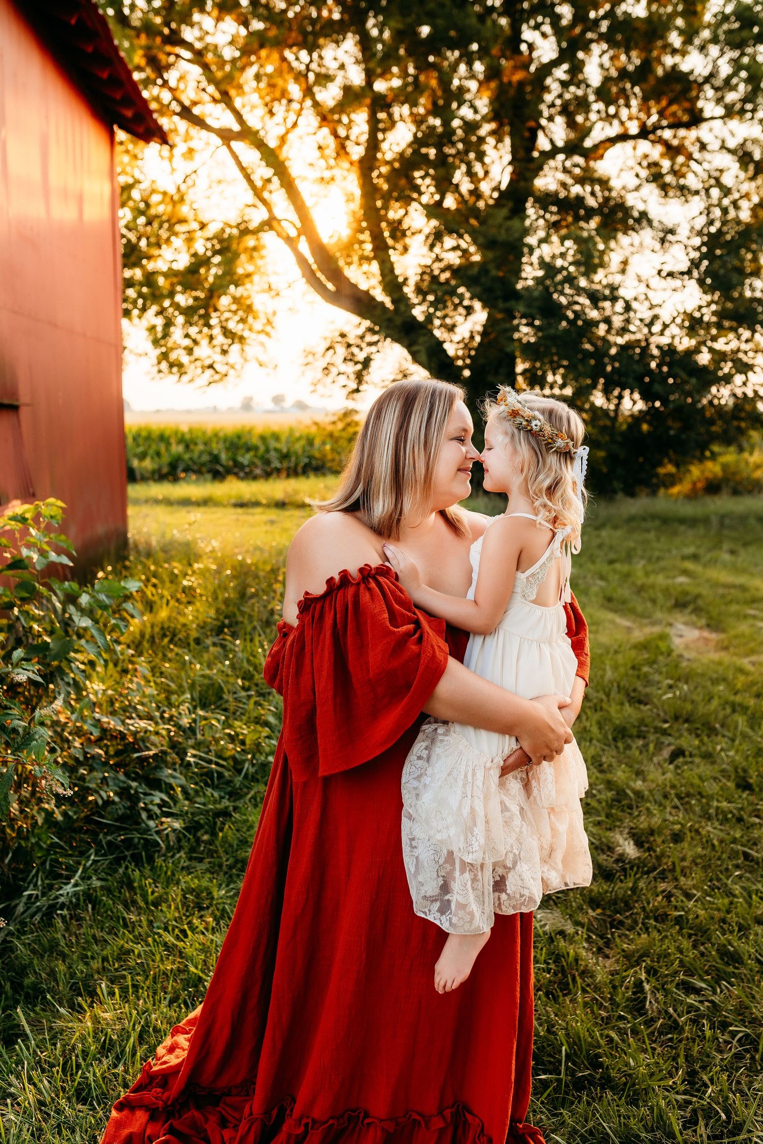 A mother and child share an intimate moment in a flowing red dress at sunset.