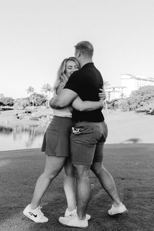 Couple embracing on a grassy golf course with a lake in the background.