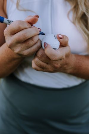 Close-up shots of hands holding and writing on a golf ball.