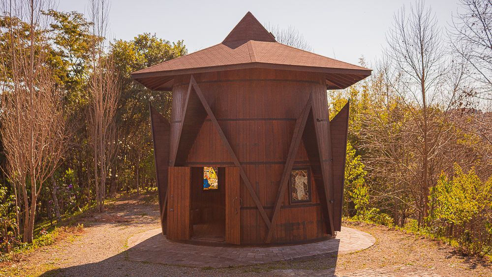 Small wooden chapel shaped like wine barrel in vineyard landscape, photographed by Piret Victoria Ribas.