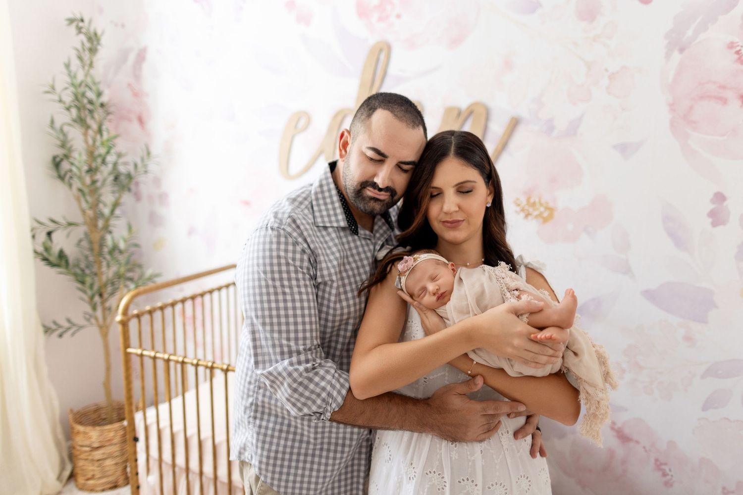 Tender family moment in nursery with pink floral wallpaper and wooden crib.