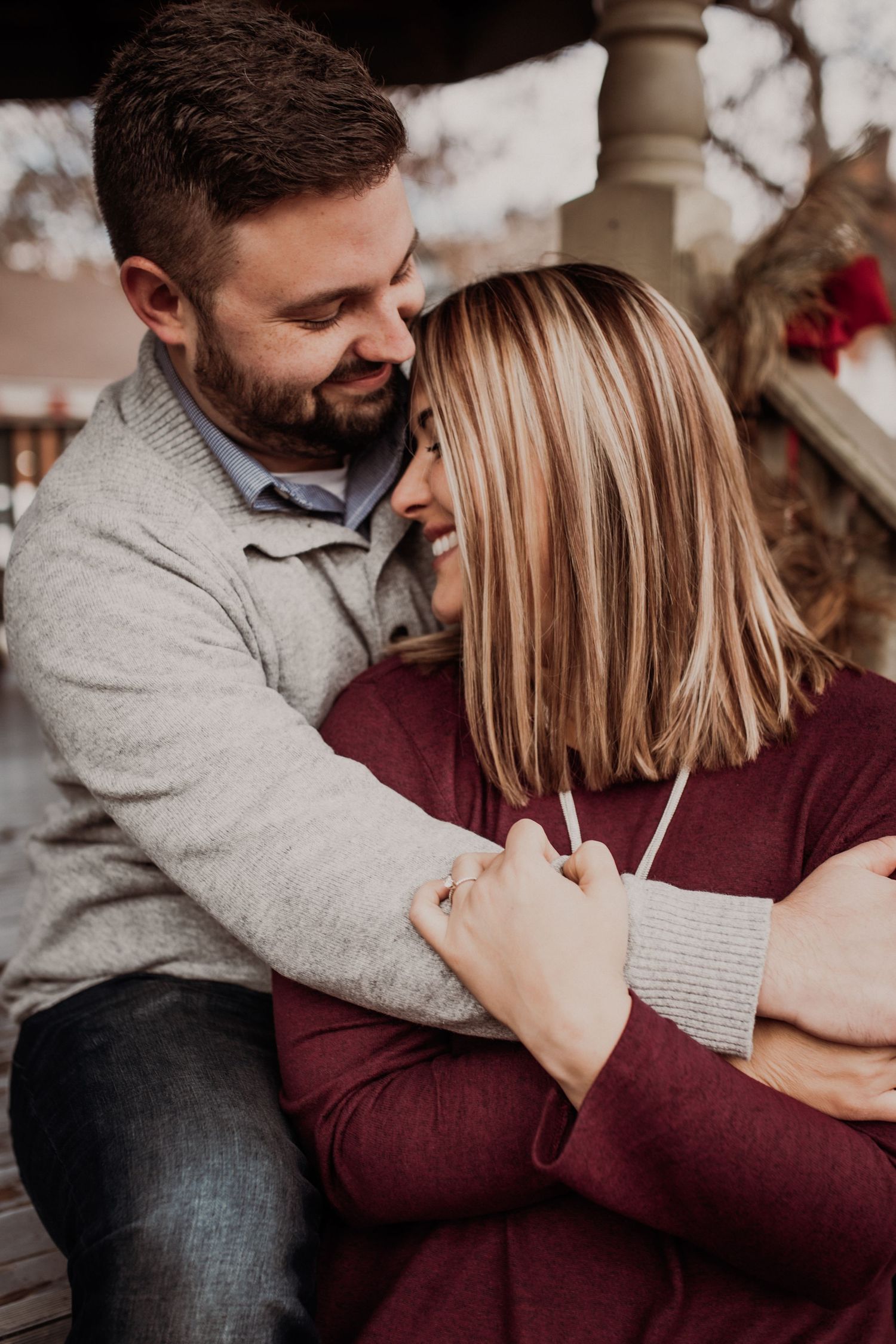 Cozy autumn portrait of couple embracing on porch in casual sweaters.