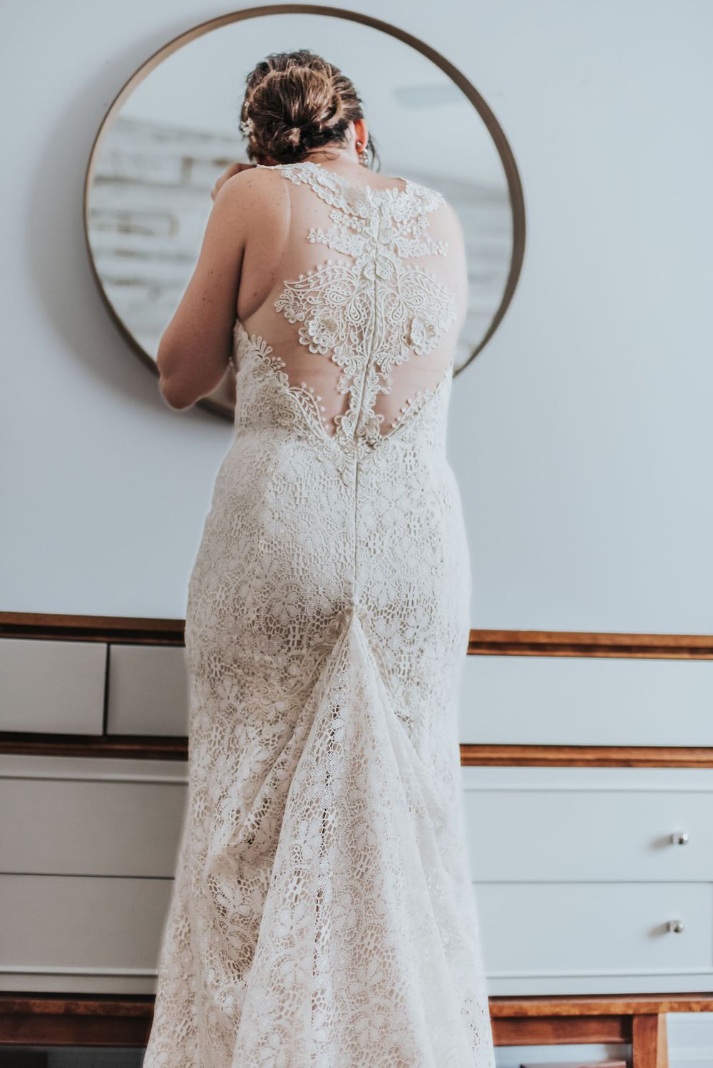 A woman prepares for her wedding and puts her earrings on as she looks in the mirror.