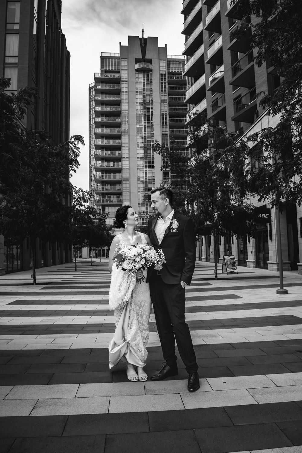 Bride and groom stand in downtown Burlington Ontario looking at one another with a tall building in the background.