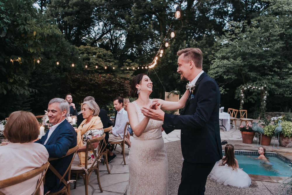 Newly wed couple dancing together with family watching in the back.