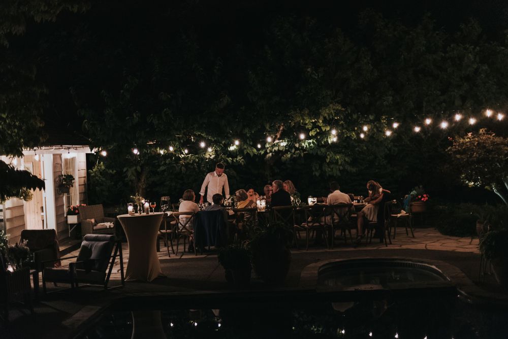 Evening photograph of an intimate backyard wedding dinner with lights strung above.