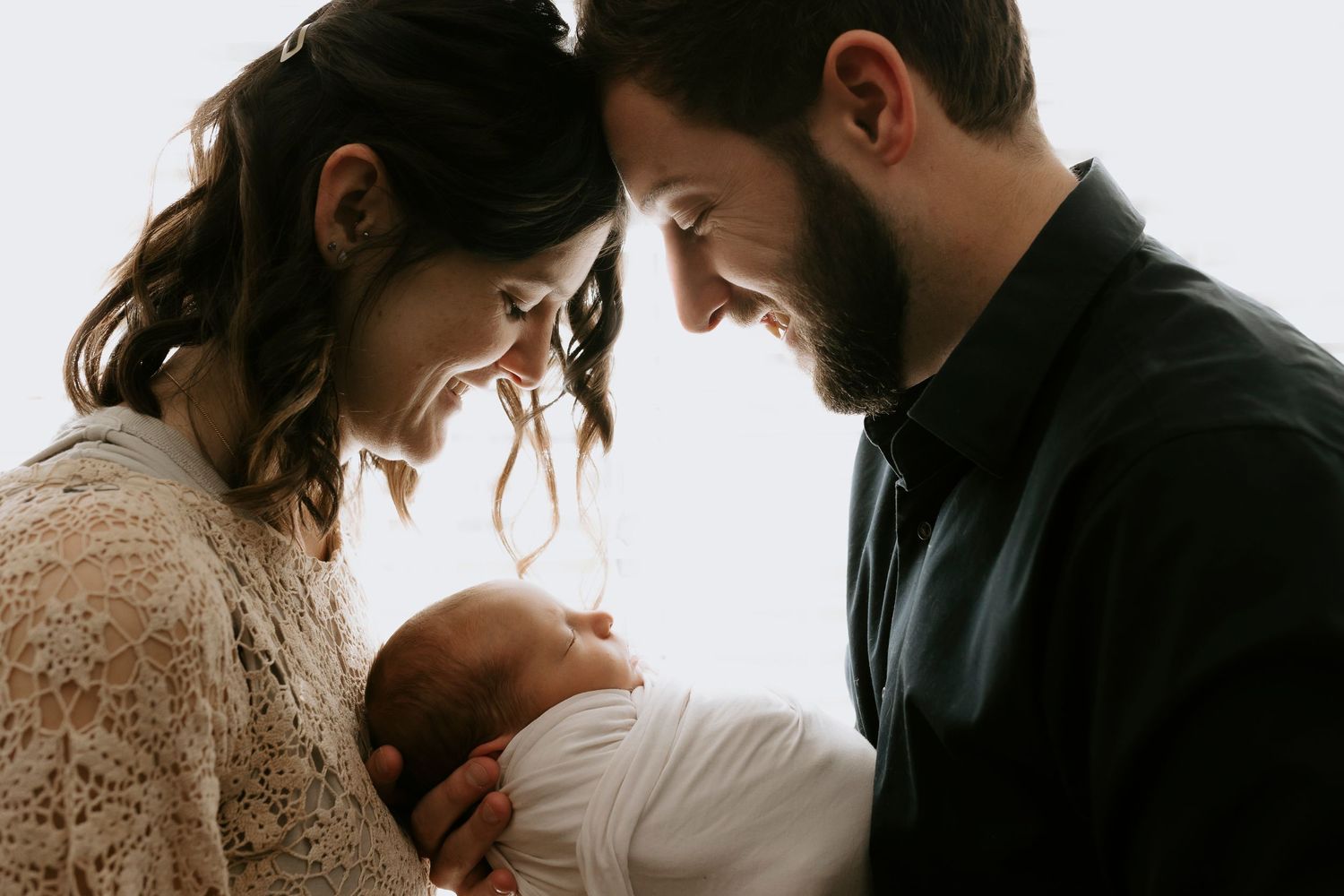 A loving family photoshoot in a cozy bedroom with warm neutral tones and natural light.