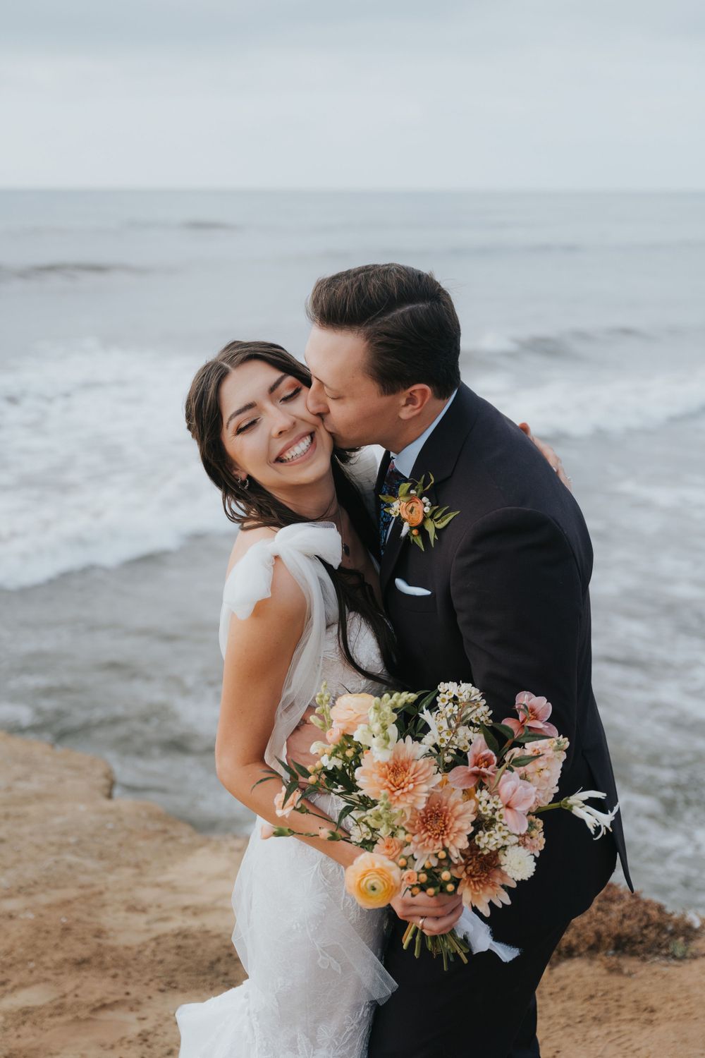 A groom kisses his bride during their destination summer elopement to Sunset Cliffs in San Diego, California.
