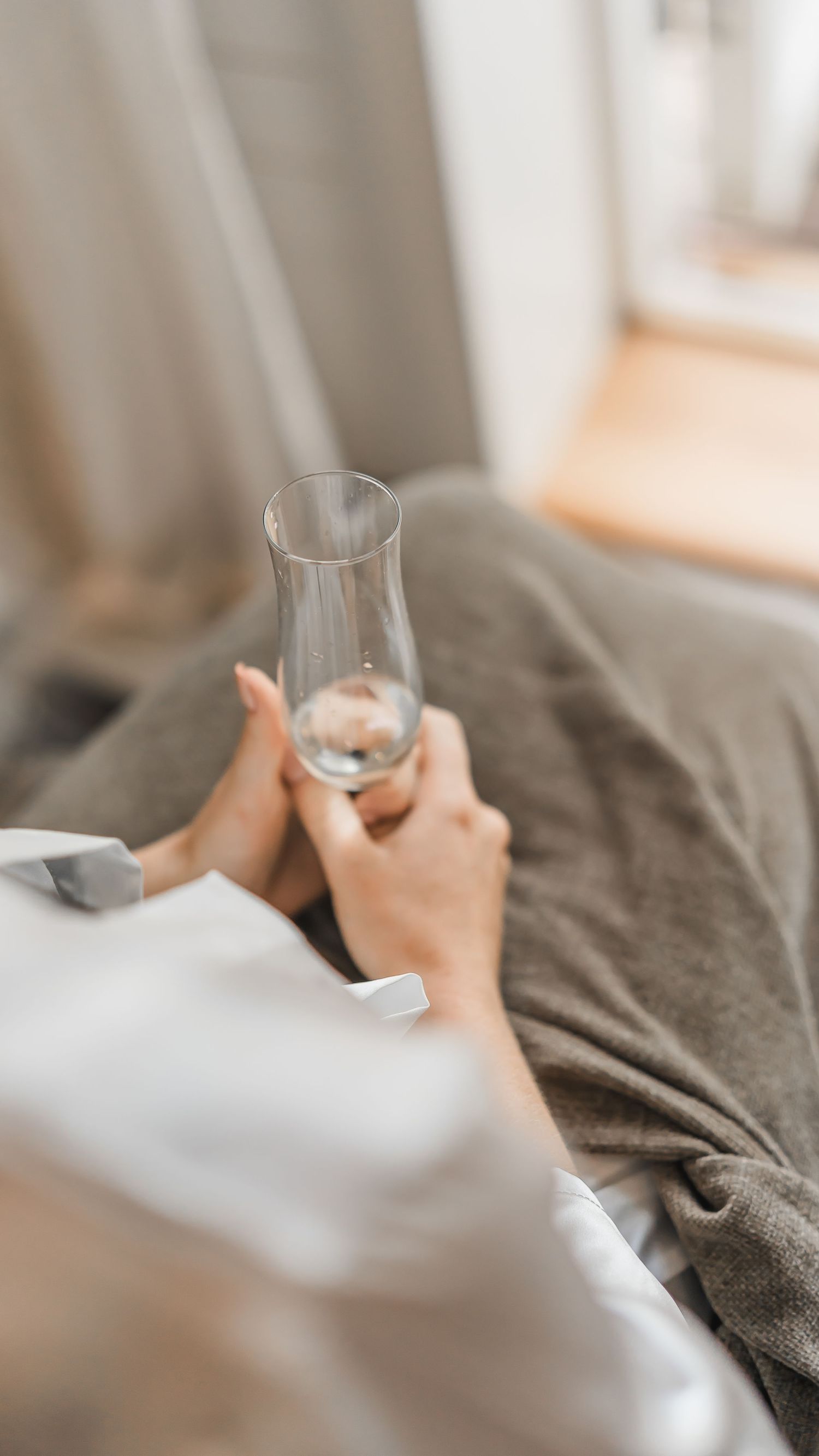 Bride in a white satin robe relaxing and holding an empty champagne glass while getting ready.