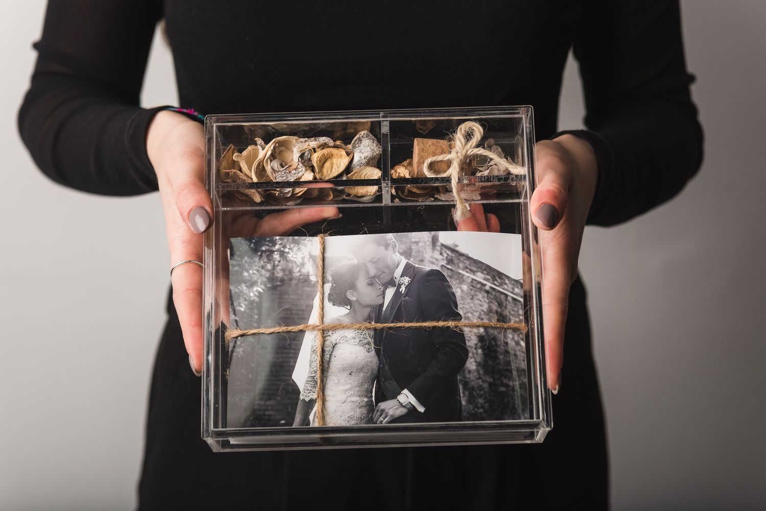 Hands holding a clear acrylic box containing vintage-style photographs and cork decorations.