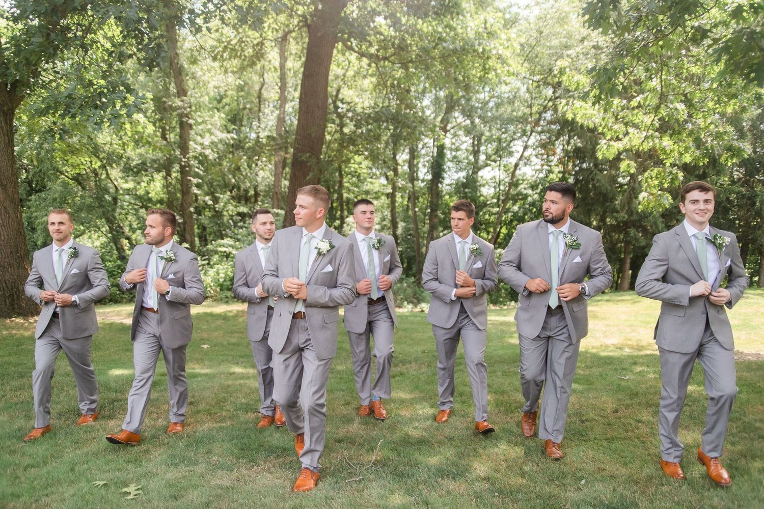 Groomsmen in matching gray suits strike fun poses on grass.