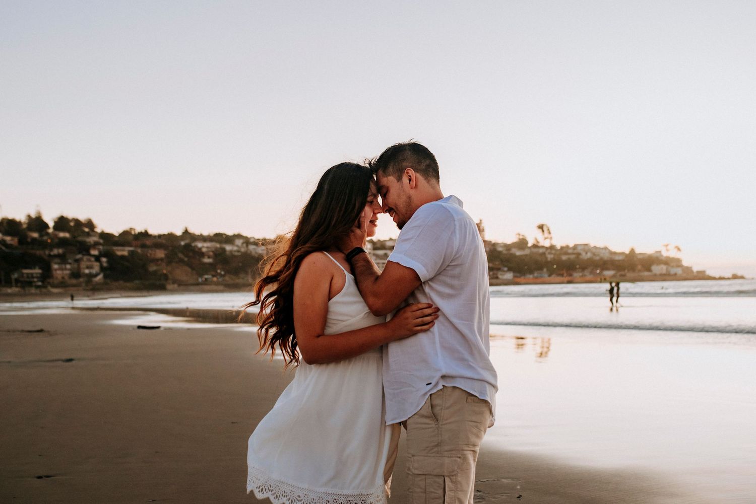 Romantic couple sharing an intimate moment on a sandy beach at sunset with ocean waves in the background.