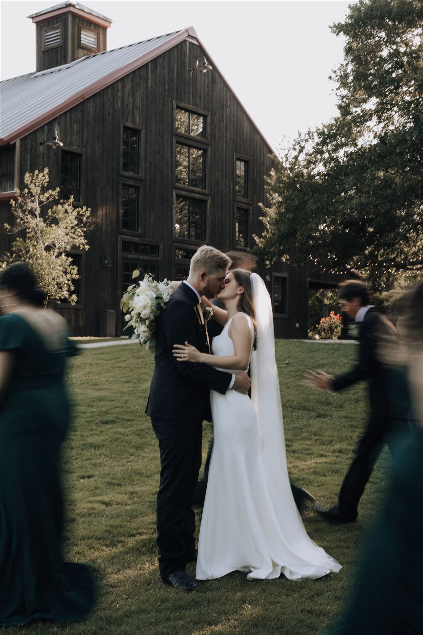 Romantic moment captured outside rustic barn venue with guests in motion.