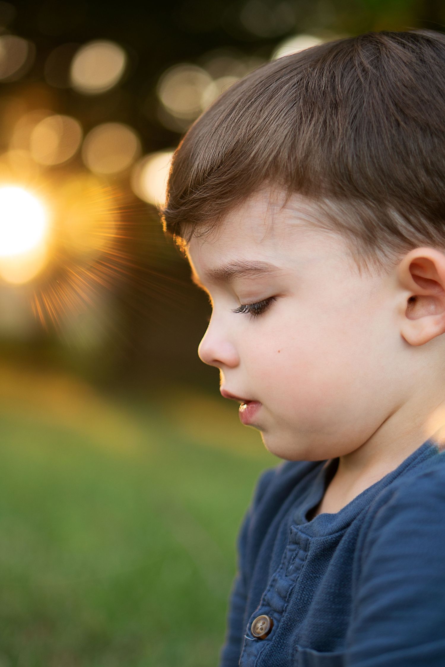 sun rays peek through trees in closeup profile portrait of young boy
