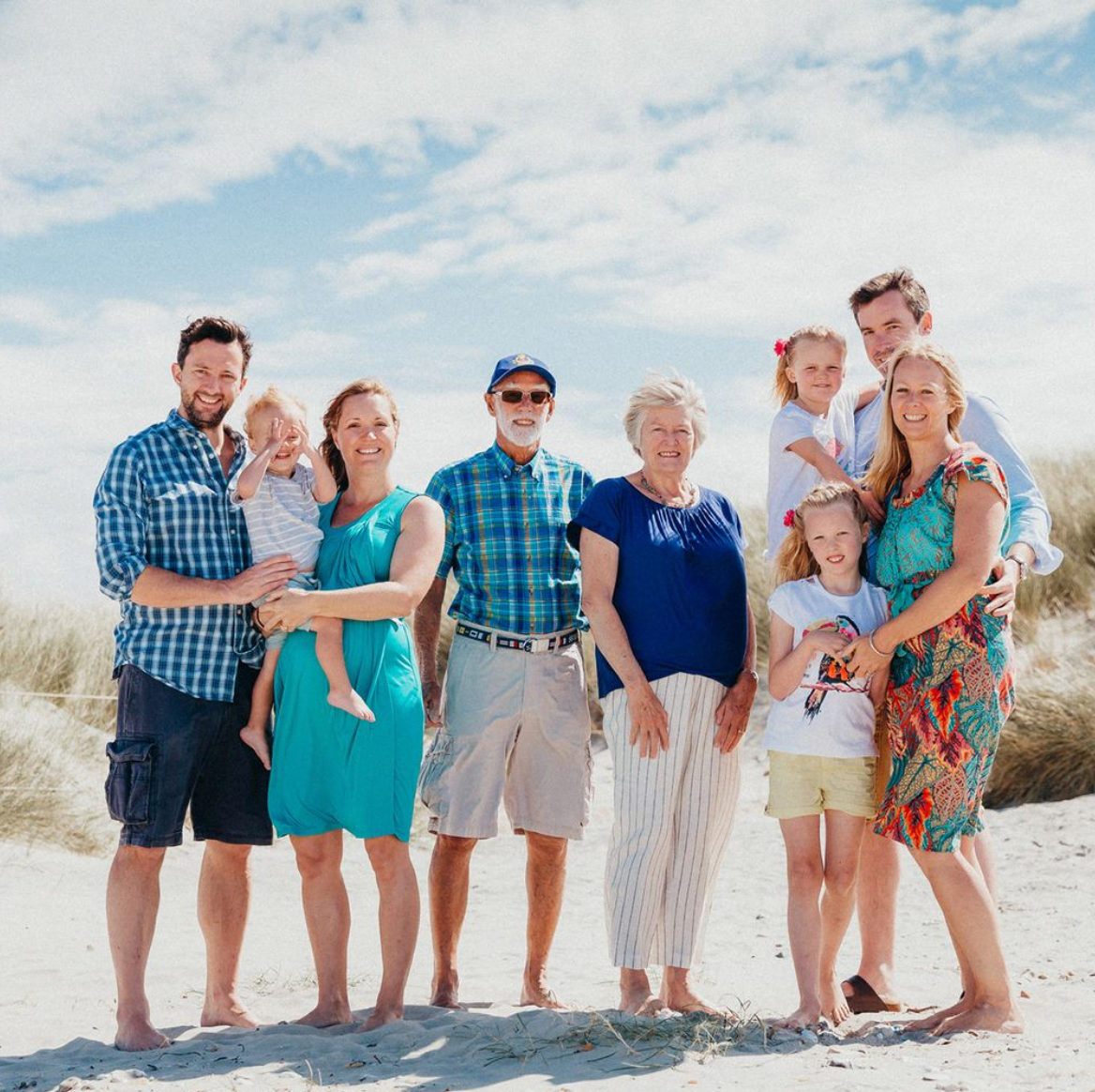 Extended family group posed together on sandy beach dunes on a bright summer day during a family beach photoshoot