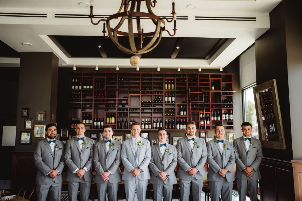 Groomsmen lineup in grey suits beneath rustic chandelier in elegant bar setting.