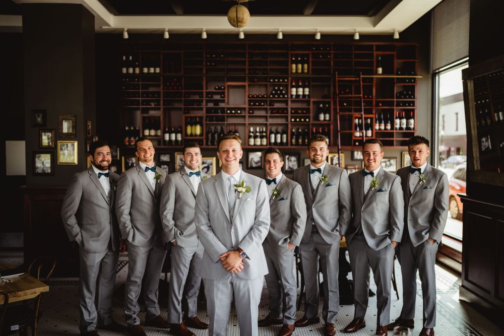 Wedding party in matching grey suits standing in front of a built-in bar display.