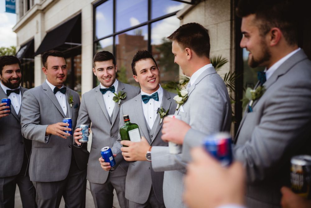 Groomsmen in grey suits enjoying drinks and conversation at a wedding celebration.