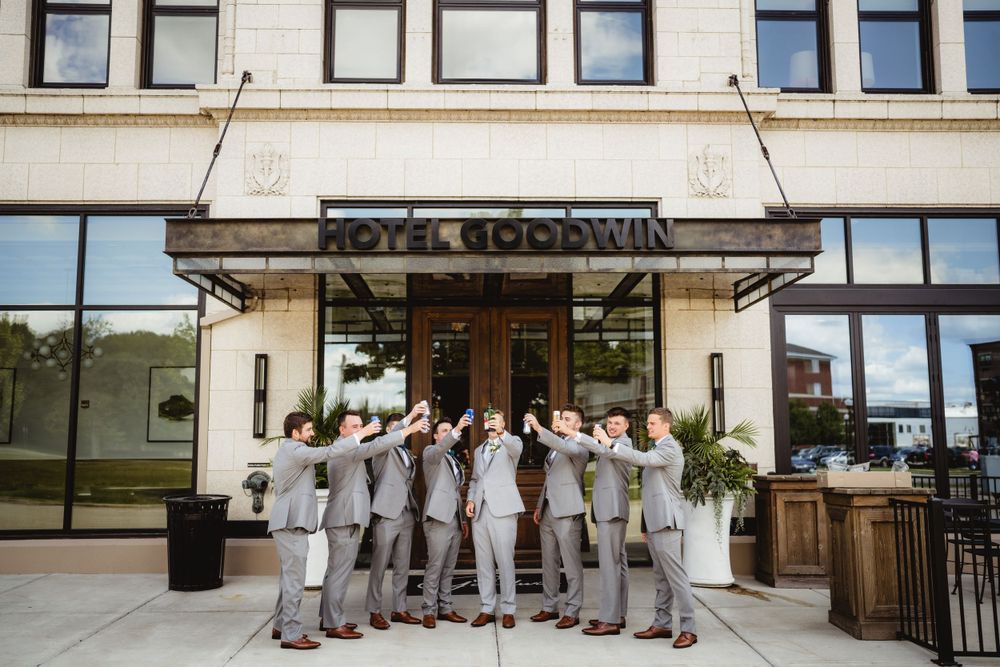 Wedding party wearing grey suits poses together in front of Hotel Goodwin entrance.