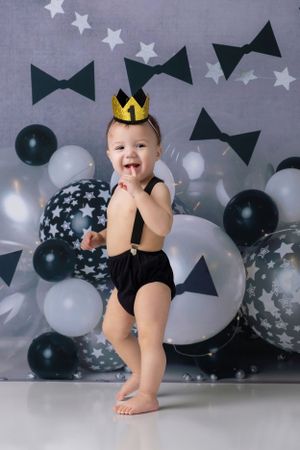 Playful pose against grey background with black and white balloons and bow tie decorations.