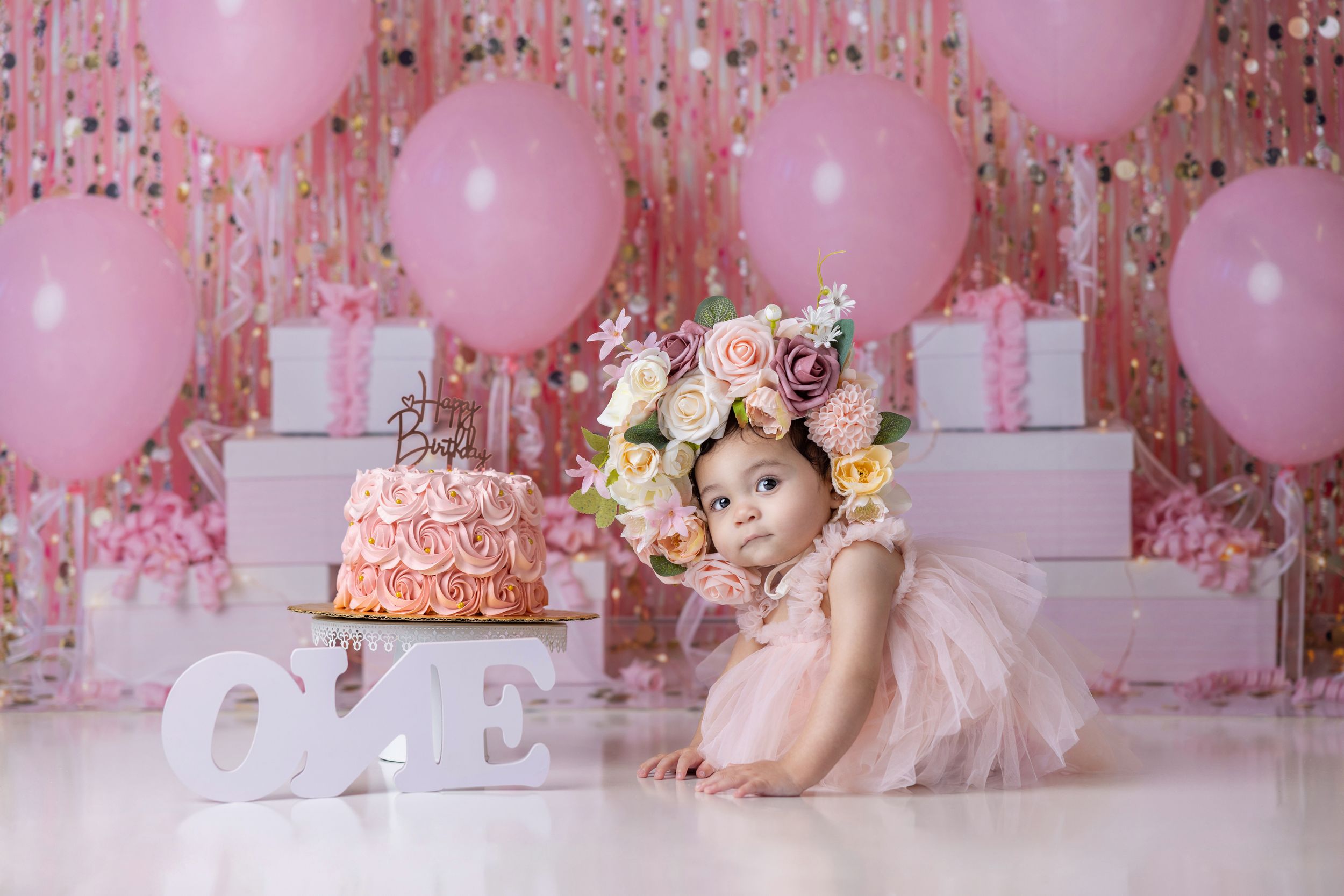 Elegant pink and white first birthday setup with floral crown and ombre ruffled cake.