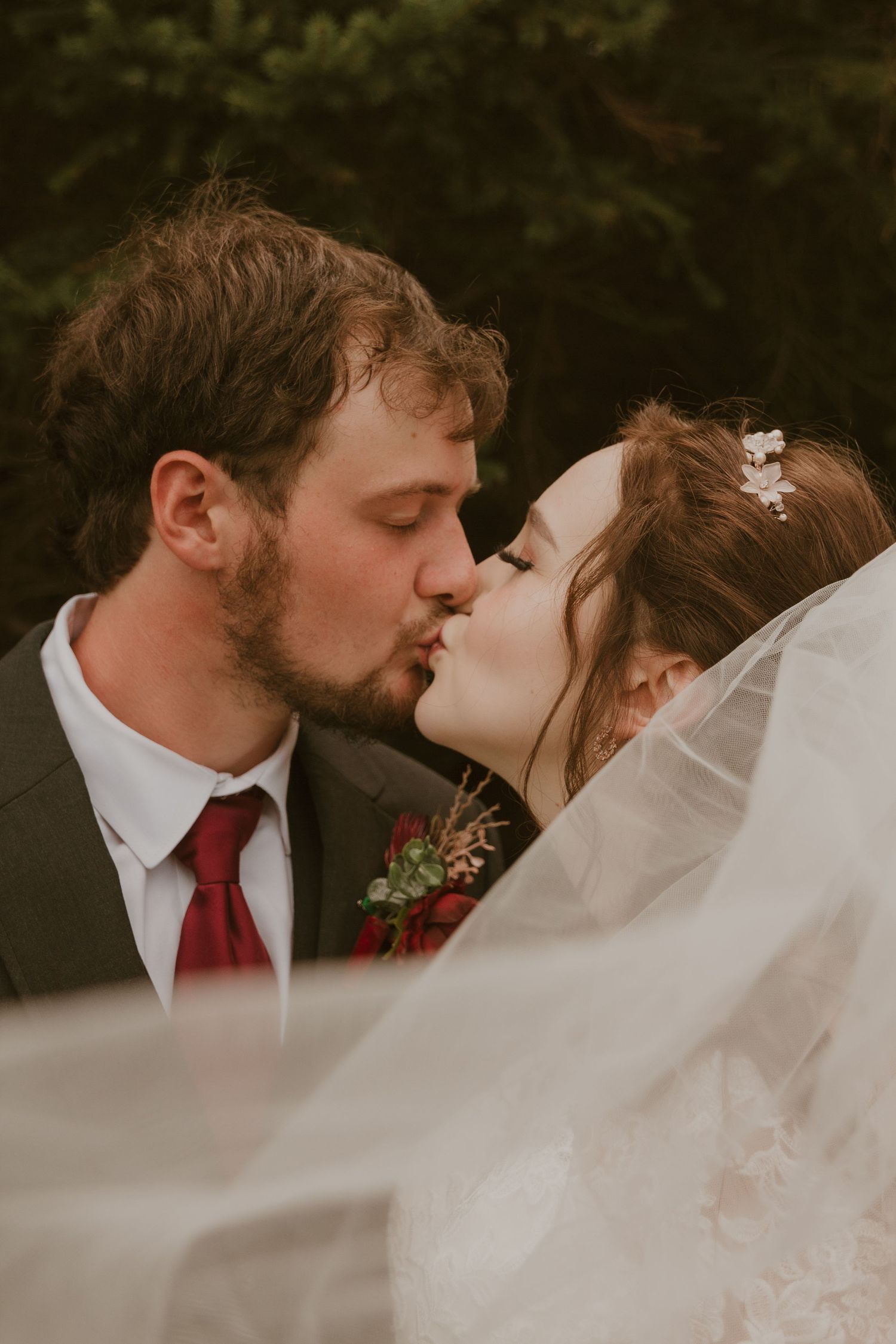 Romantic wedding portrait of couple kissing with flowing veil in soft lighting.