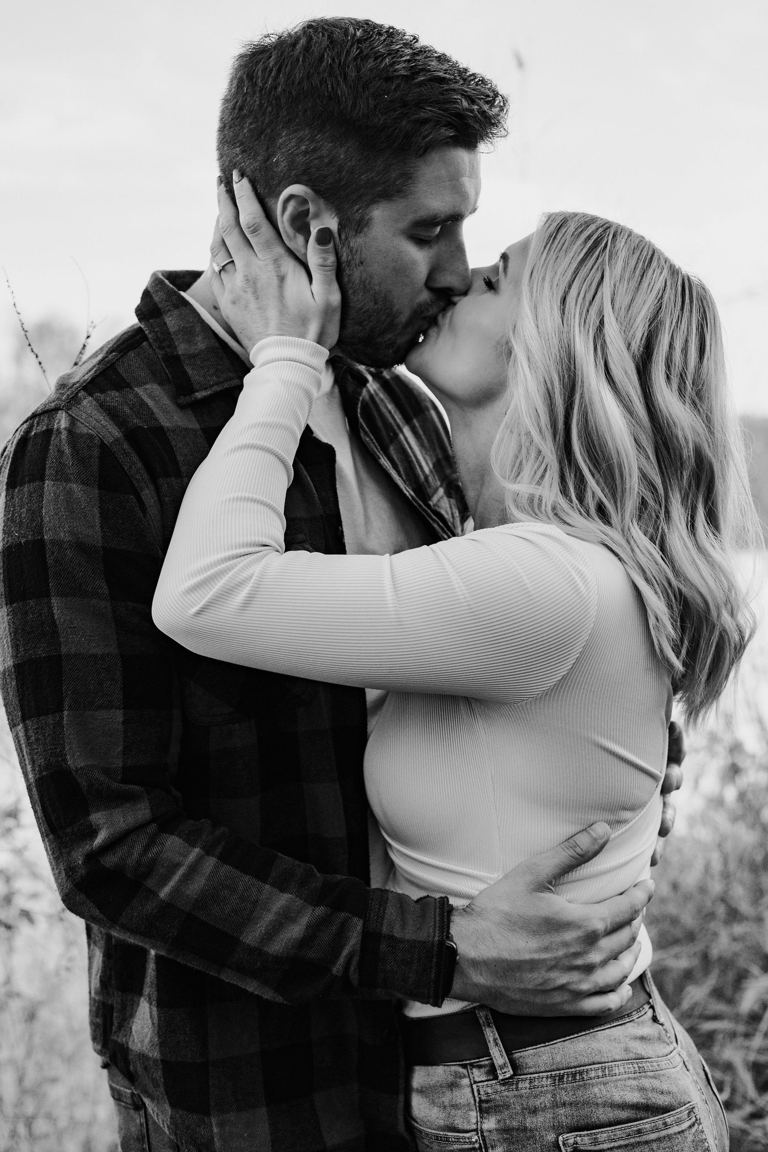 Black and white romantic photo of couple sharing a passionate kiss outdoors.