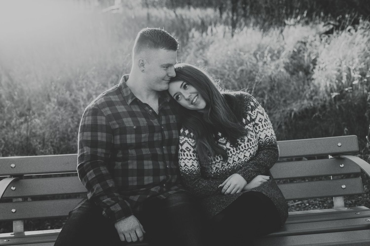 Black and white photo of couple sitting on bench, woman leaning on mans shoulder.