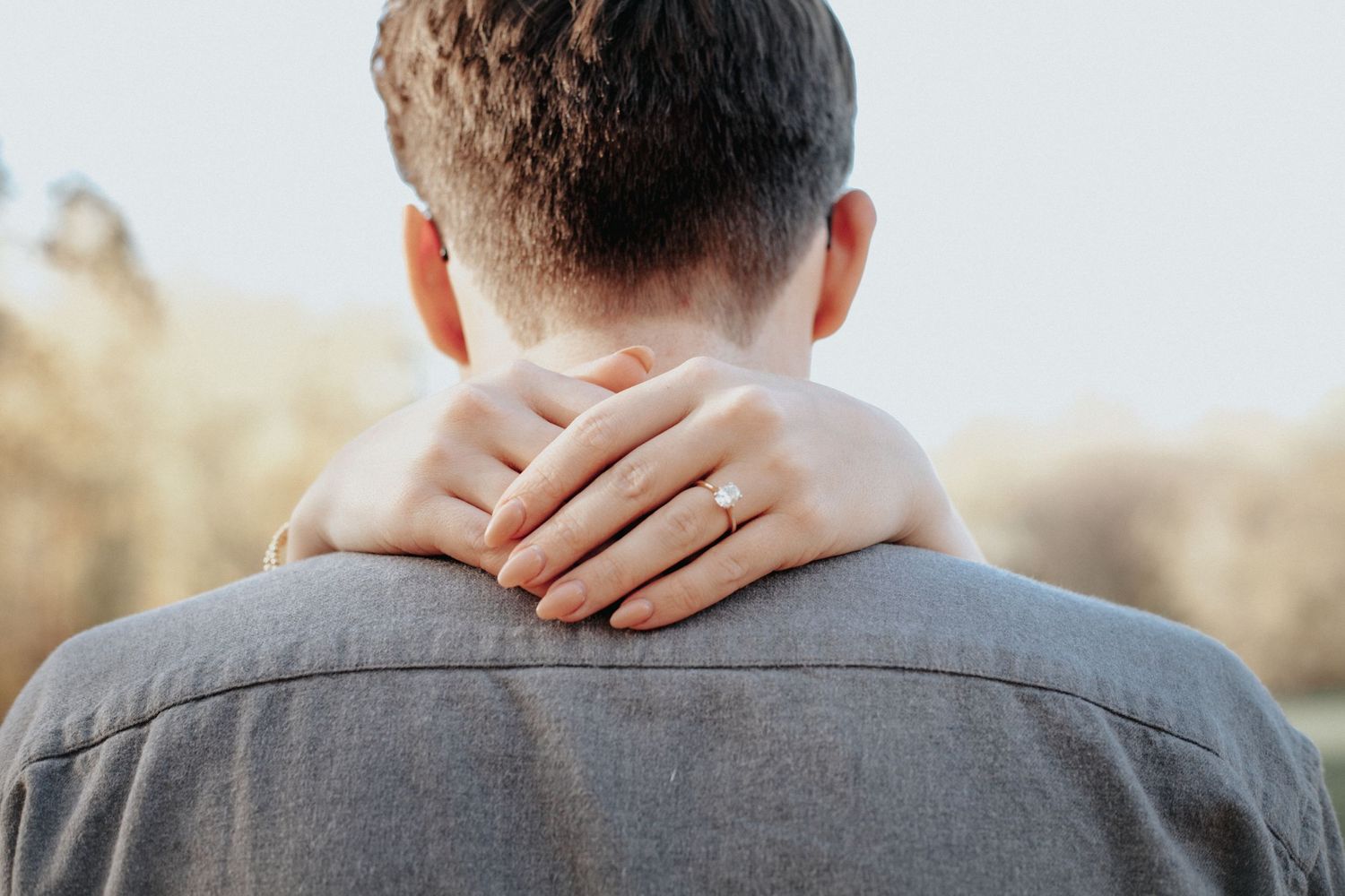 A woman places her hand on a man's neck in a tender outdoor embrace.
