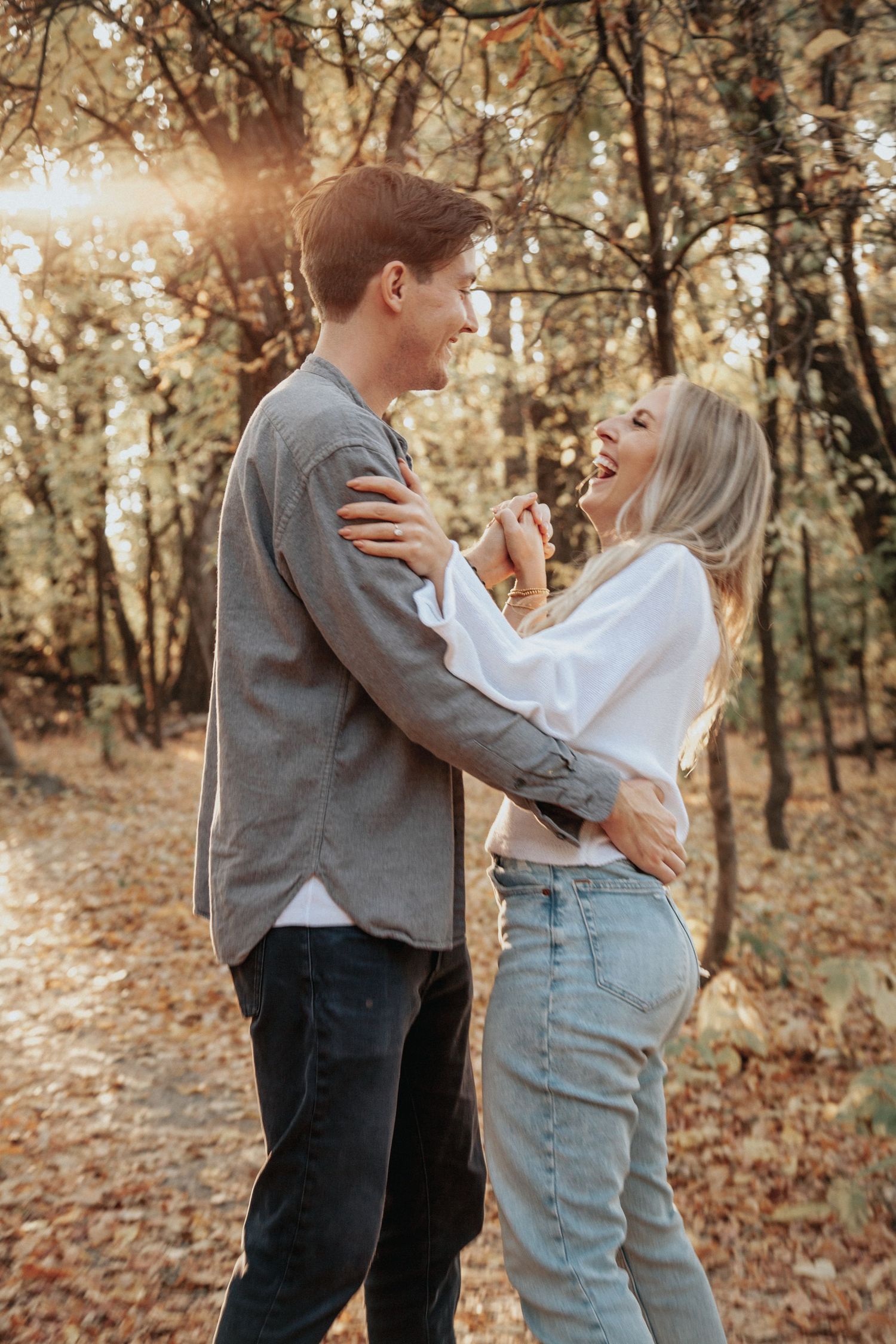 A happy couple laughs and embraces in a sunlit autumn forest setting.